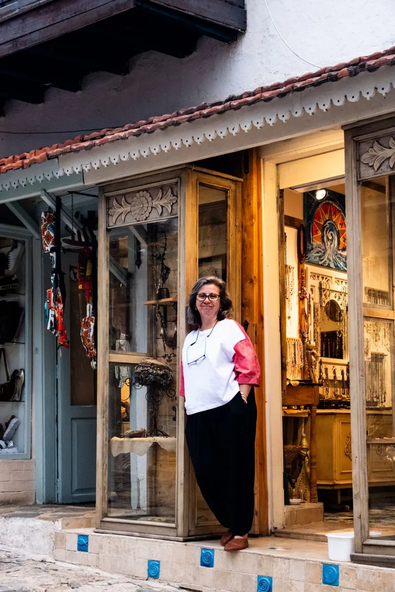 A friendly shop owner stands outside a rustic artisan store, showcasing crafts and souvenirs.